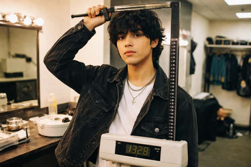 Ivan Cornejo standing against a height measurement wall Ivan Cornejo standing against a height measurement wall chart, wearing casual clothing, with measurement markings visible beh